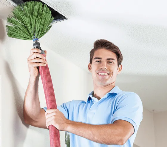 Technician holding a cleaning tool with a broom, performing expert HVAC duct cleaning services.
